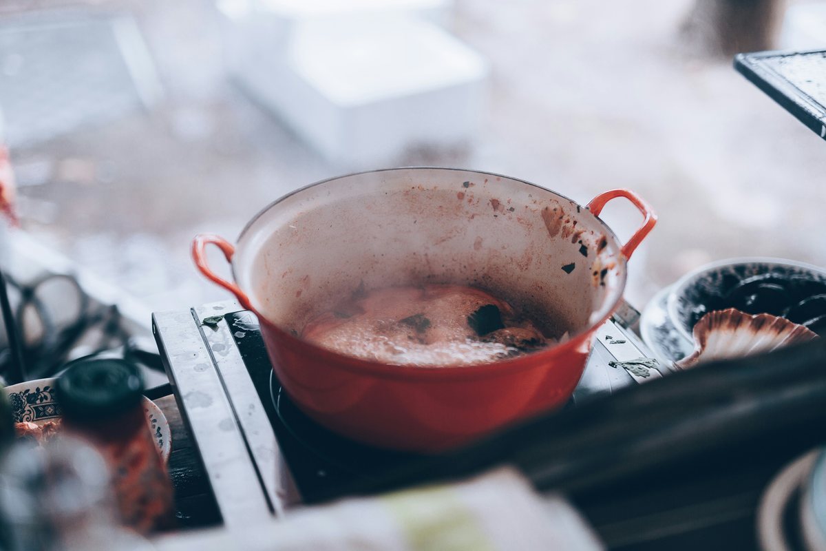 A red cooking pot simmering with dark marks around its inner rim.