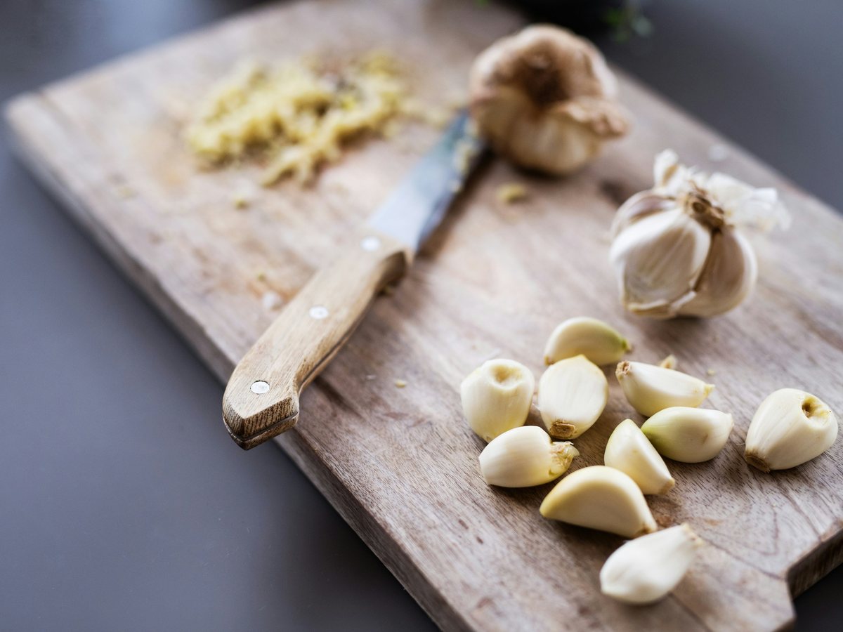 Peeled garlic cloves, a knife, and minced garlic on a wooden board.