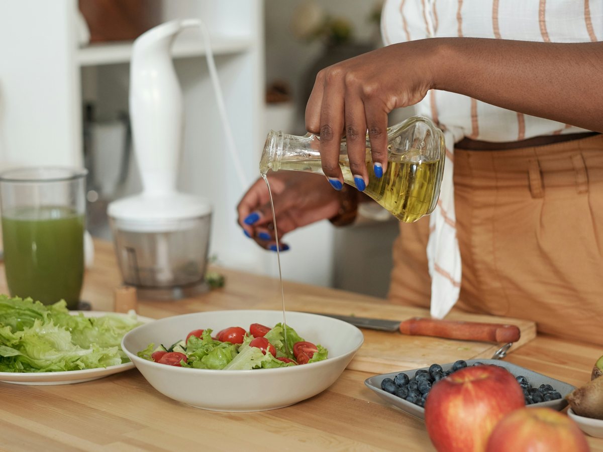 Olive oil being poured over a bowl of salad leaves and tomatoes.