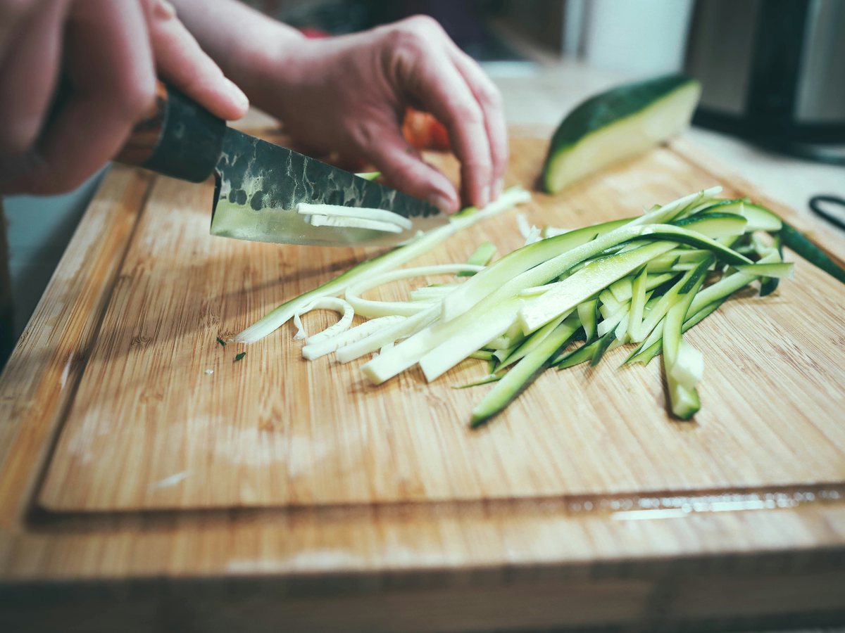 A cook cuts a courgette into thin strips on a wooden board.