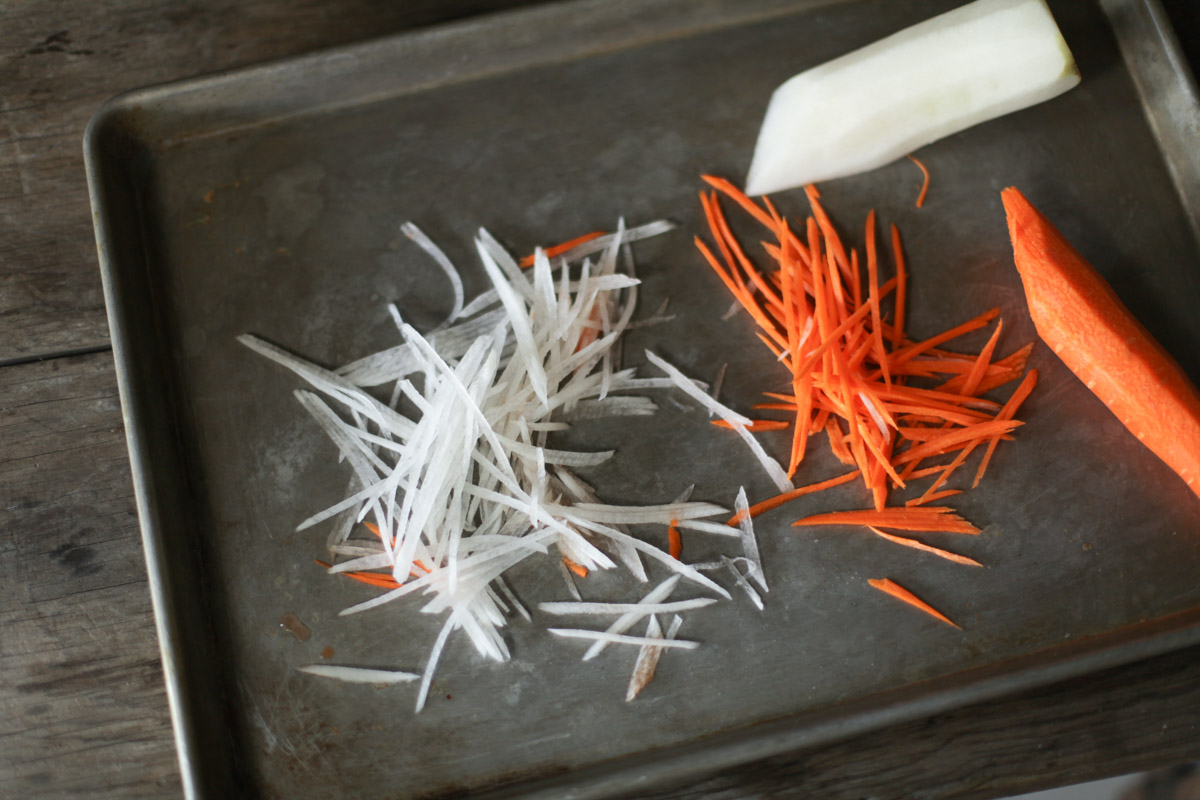 Thin matchsticks of carrot and daikon radish on a metal tray.