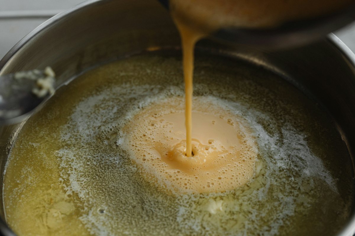 A yellow sauce being poured into a pan of melted butter.