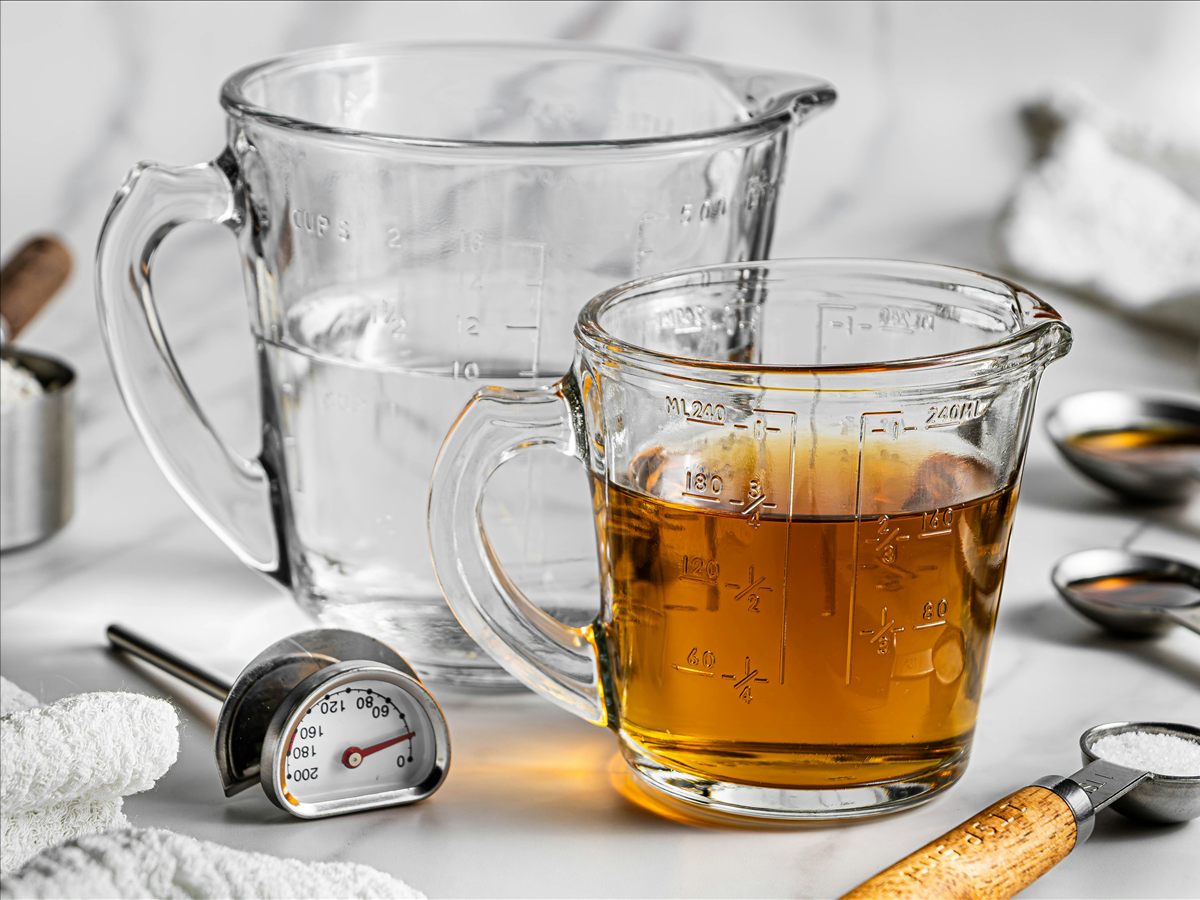 Two marked glass measuring jugs holding clear and amber liquids beside measuring spoons.