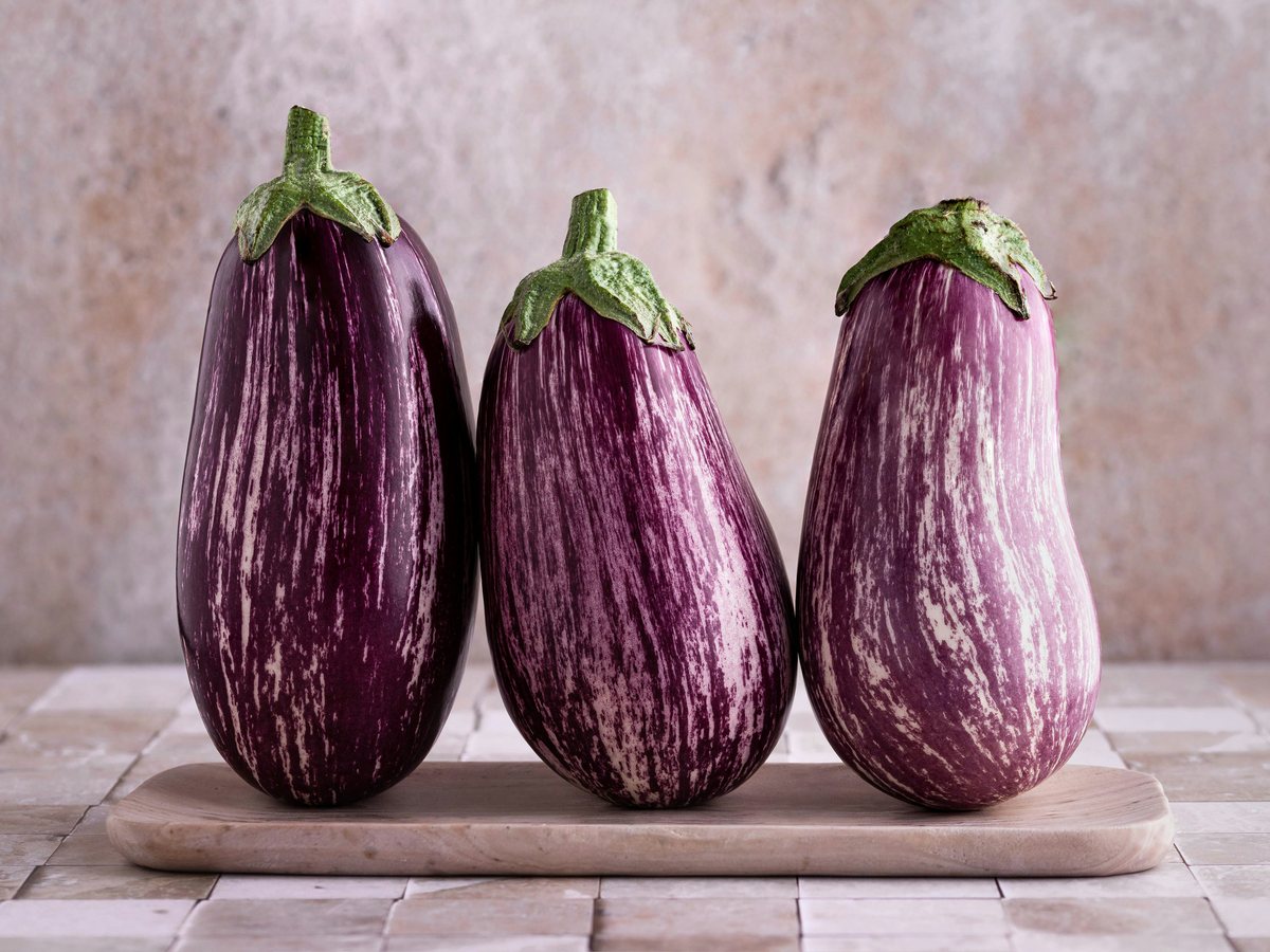 Three striped purple aubergines on a wooden board.