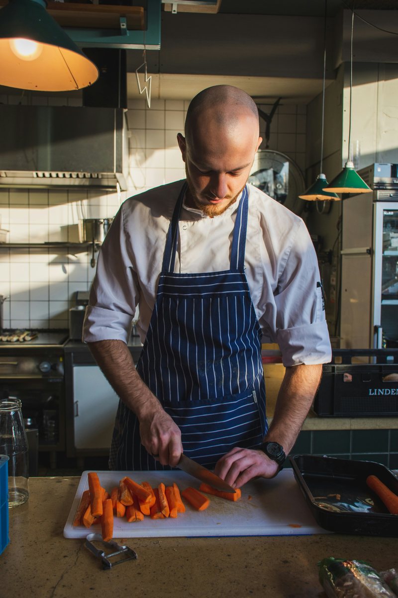 A chef cuts carrots with a knife on a chopping board.