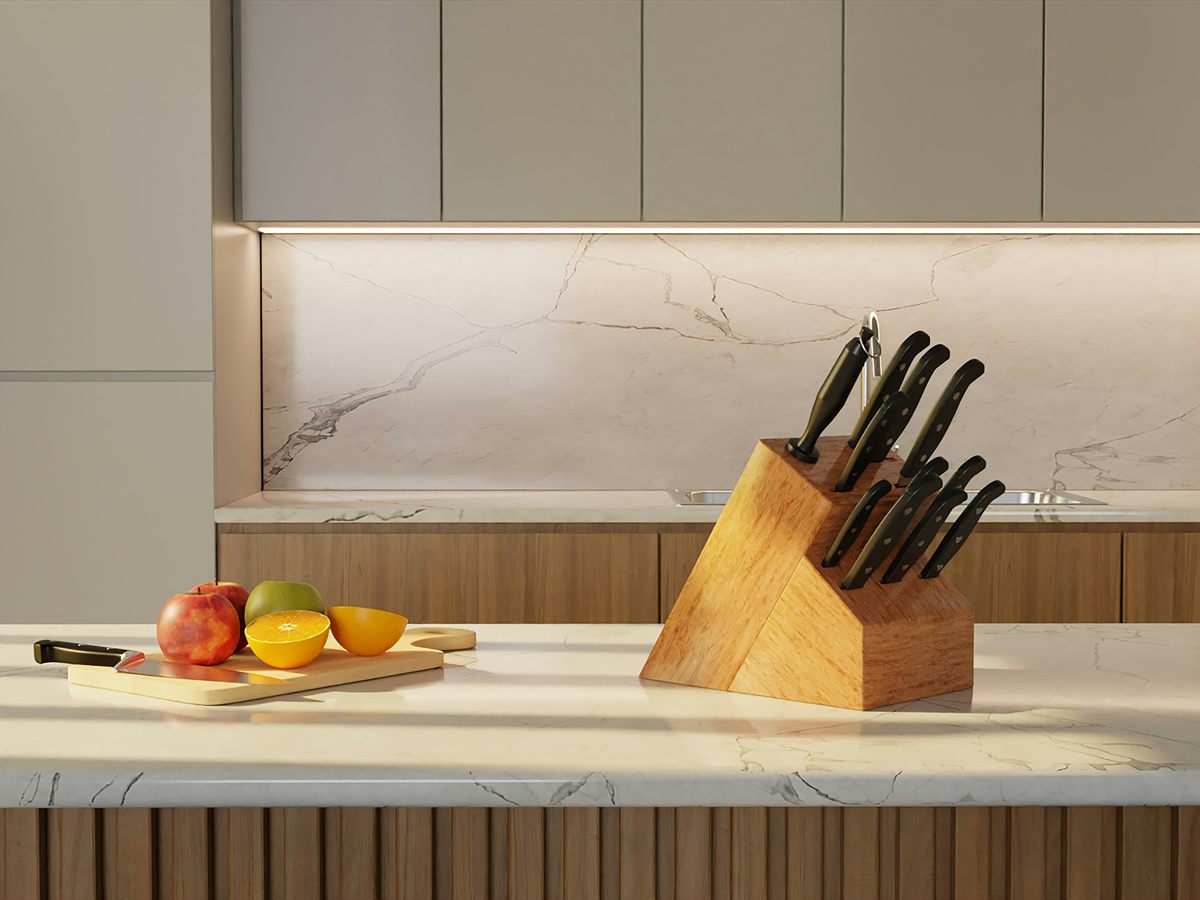 A wooden block of kitchen knives beside fruit on a bright kitchen counter.
