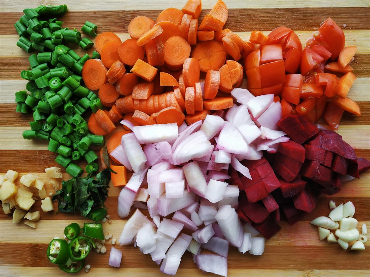 Piles of chopped vegetables in different shapes on a wooden cutting board.
