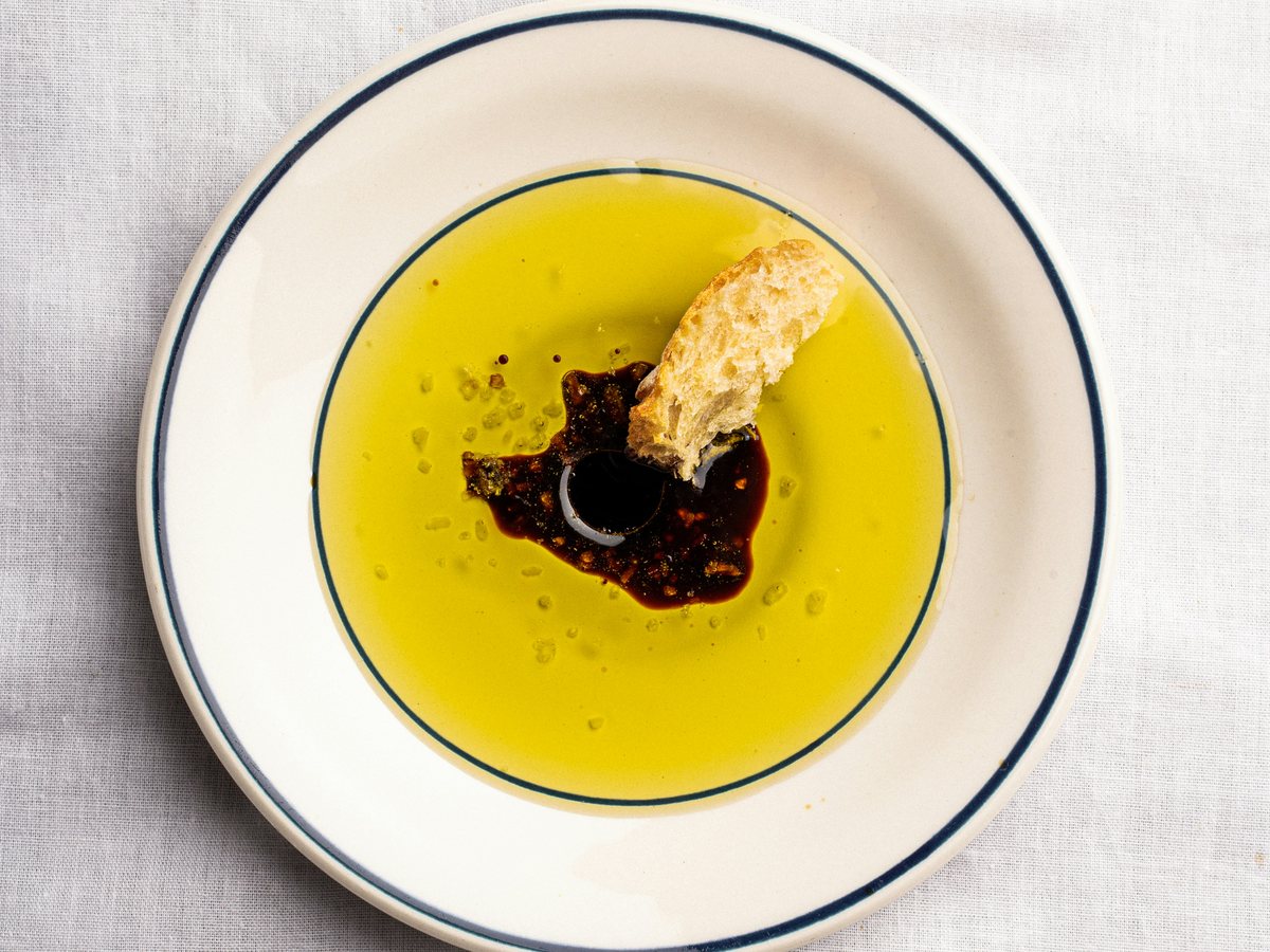 Separate pools of olive oil and balsamic vinegar on a white saucer with bread.