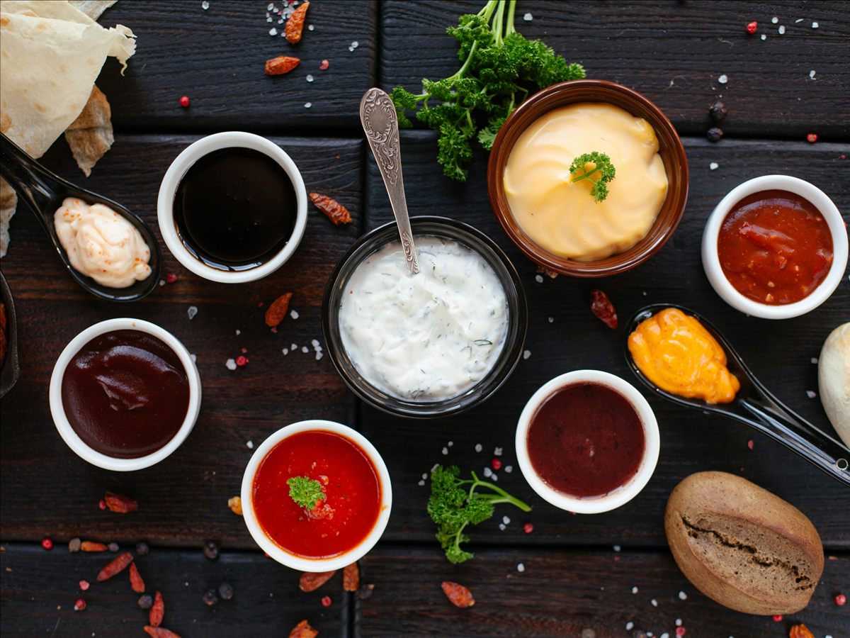 Assorted red, white, yellow, and brown sauces in bowls on a dark wooden table.