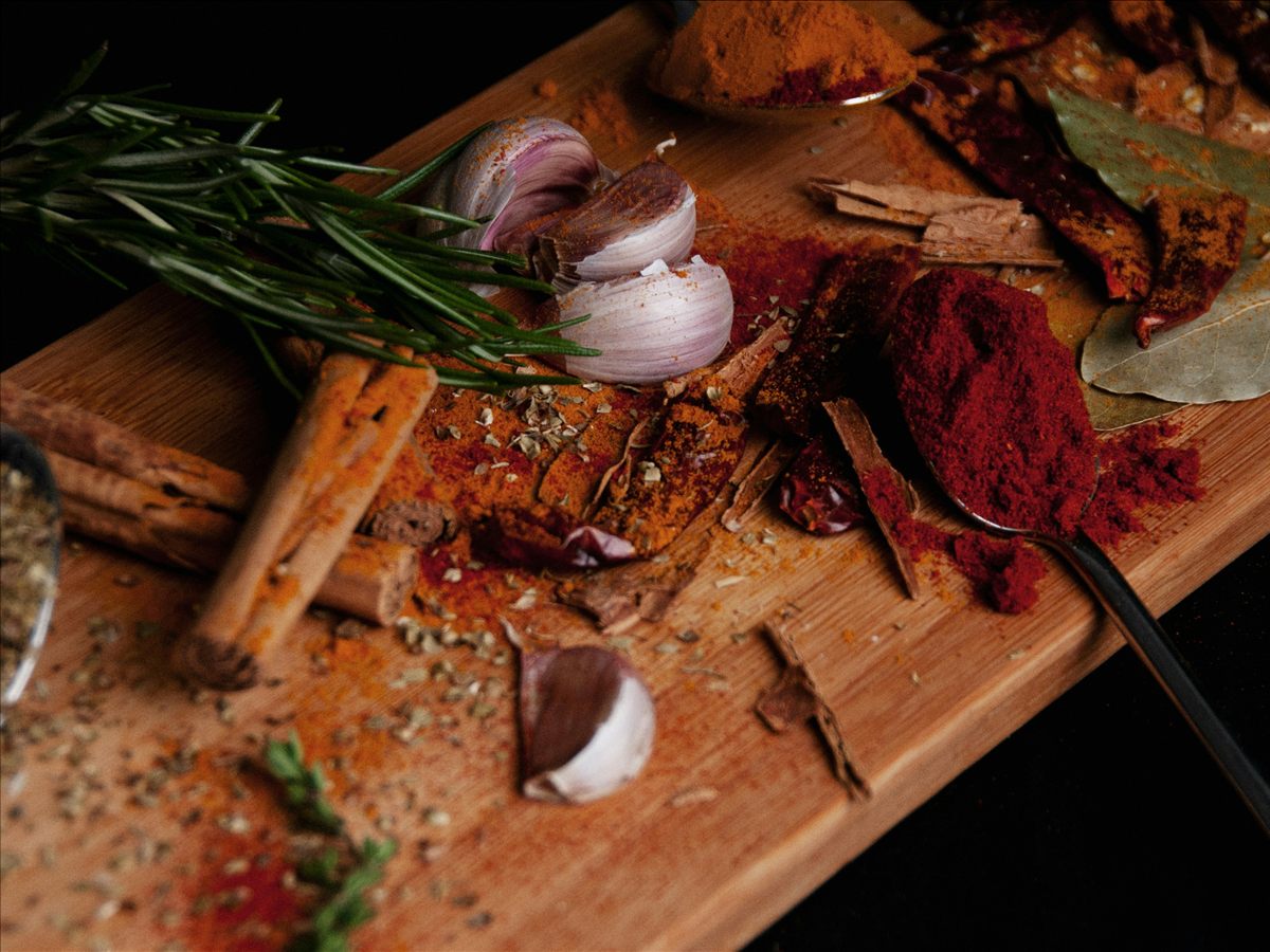 Garlic, rosemary, cinnamon, bay leaves, and spices on a wooden board.